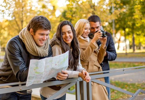 travel, vacation, technology, tourism and friendship concept - group of smiling friends with digital photo camera and map in city park