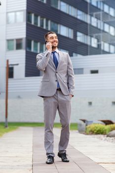 business, technology and people concept - smiling businessman with smartphone talking over office building