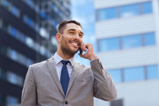 business, technology and people concept - smiling businessman with smartphone talking over office building