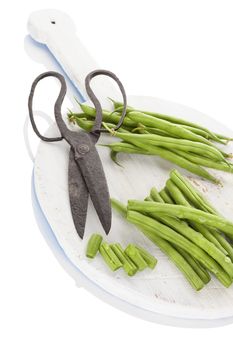 Fresh green beans with water drops on wooden chopping board with vintage scissors isolated on white background. Healthy eating. 