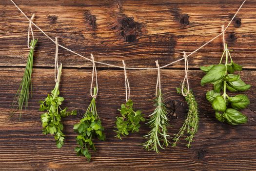 Culinary herbs. Aromatic herbs, basil, coriander, parsley, chive, mint and rosemary hanging on string on old country style wooden background. 