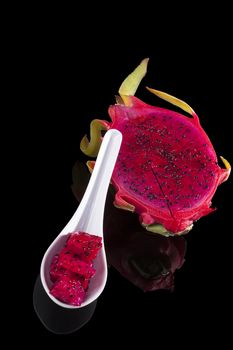 Dragon fruit pieces on spoon isolated on black background. Tropical fruit salad.