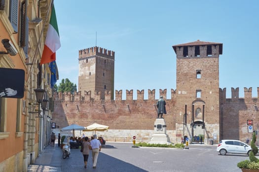 VERONA, ITALY - JULY 11: Pedestrians in front of Castelvecchio castle, with Italian flag in the foreground. July 11, 2015 in Verona.