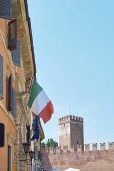 Italian flag billowing in the window, with Castelvecchio tower in the background.