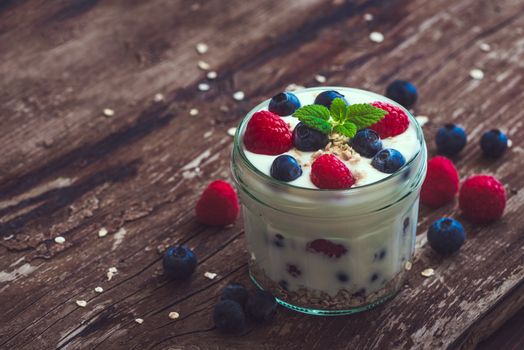 Serving of Yogurt with Whole Fresh Blueberries, Raspberries and Oatmeal on Old Rustic Wooden Table with Copyspace