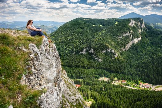 Young woman is sitting at the edge of cliff in mountains. Lacu Rosu AKA Red Lake area, Carpathians, Romania