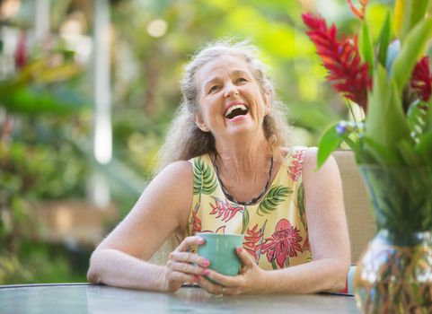 Joyful senior aged woman with mug laughing outdoors