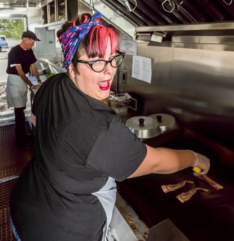 Smiling pink haired chef grills bacon in a food truck