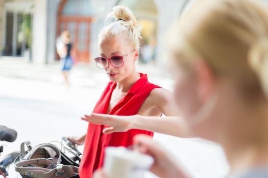 It is nice to see you. It has been a while. Two happy young female friends enjoying a conversation on a city street sidewalk at random after work encounter. Pleasant free time socializing.