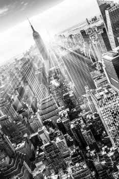 New York City. Manhattan downtown skyline with illuminated Empire State Building and skyscrapers at sunset. Vertical composition. Sunbeams and lens flare. Black and white image.