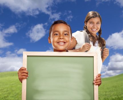 Smiling Happy Hispanic Boy and Girl In Grass Field Holding Blank Chalk Board.