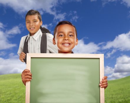 Smiling Happy Hispanic Boys In Grass Field Holding Blank Chalk Board.