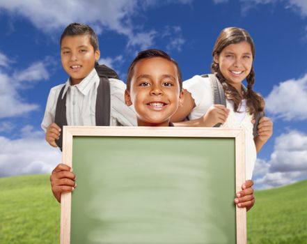 Smiling Happy Hispanic Boys and Girl In Grass Field Holding Blank Chalk Board.