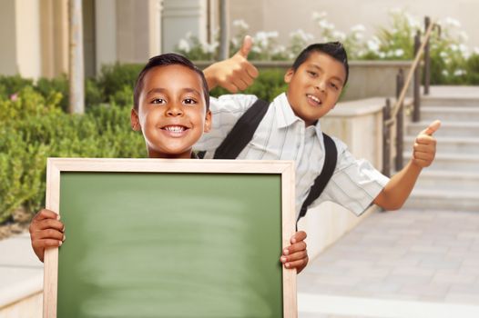 Happy Hispanic Boys with Thumbs Up Holding Blank Chalk Board Outside on School Campus.