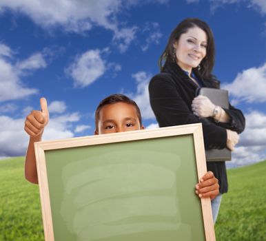 Young Hispanic Boys with Blank Chalk Board and Teacher Behind on Grass Field.