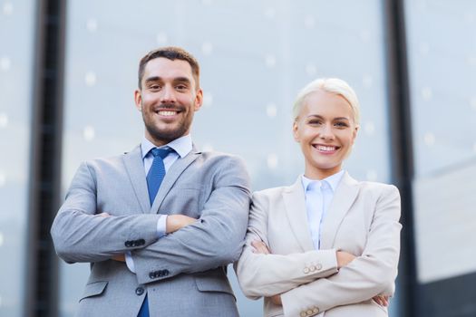 business, partnership, success and people concept - smiling businessman and businesswoman standing over office building