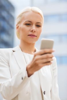 business, technology and people concept - serious businesswoman with smartphone over office building