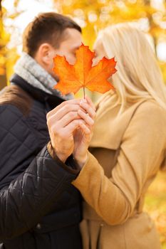 love, relationship, family and people concept - close up of couple with maple leaf kissing in autumn park