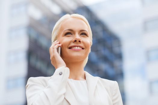 business, technology and people concept - smiling businesswoman with smartphone talking over office building