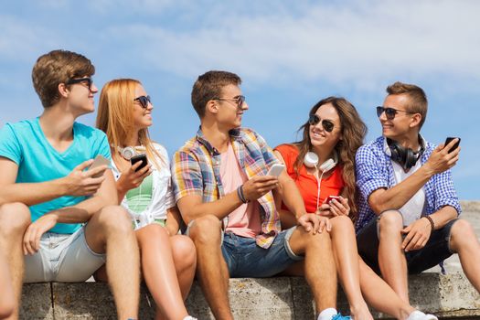 friendship, summer, technology and people concept - group of smiling friends with smartphones and headphones outdoors