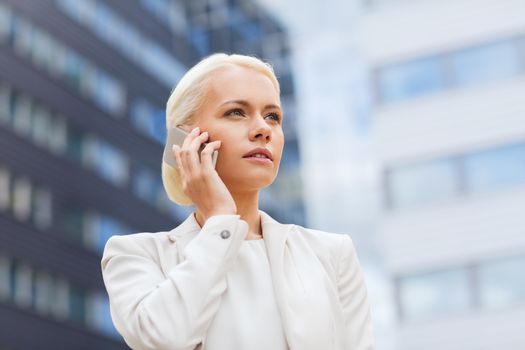 business, technology and people concept - serious businesswoman with smartphone talking over office building