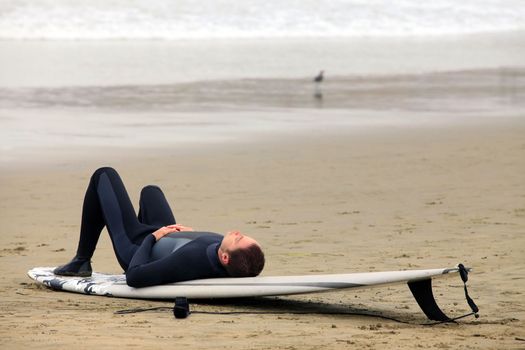 Surfer lying on a board resting on the beach
