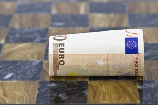 Close focus on euro currency unrolling on chess board.  Symbols of challenges in euro market, banking, and business.  