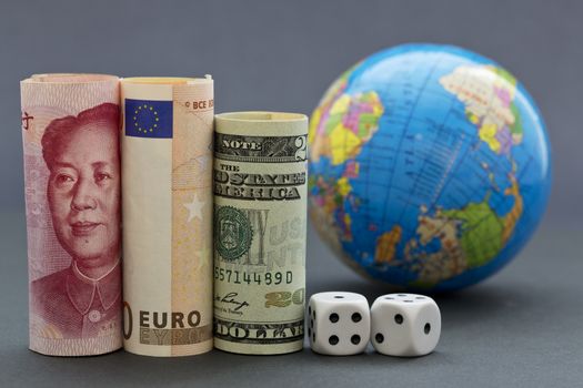 Yuan, euro, and collar next to black and white dice with globe in background.  When risks are worldwide, business and investment decision makers take into account larger, international strategies. 