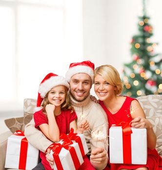 family, christmas, x-mas, happiness and people concept - smiling family in santa helper hats with many gift boxes and bengal lights