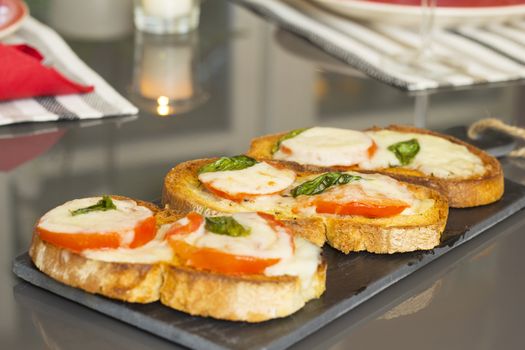 Three Beautifull and delicious italian style charcoal grilled bruschetta with tomato cheese and basil, over a slate dish isolated in a grey background.