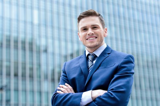Confident businessman posing with folded arms outside skyscraper