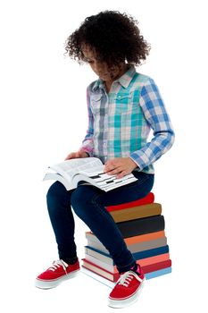 School girl sitting on stack of book and reading