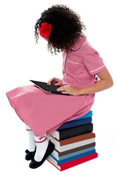 School girl sitting on books with digital tablet