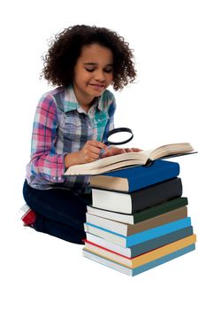 Little girl reading a book using magnifying glass