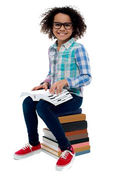 Happy girl sitting on stack of books over white