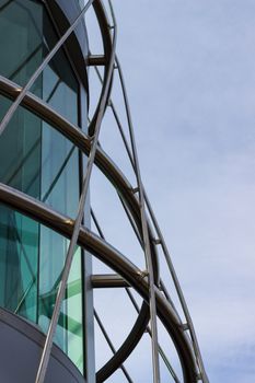 A circular Steel frame surrounding the corner of a building set against a blue white sky.