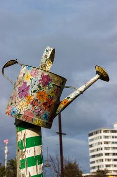 This is a highly decorated watering can, painted with colorful flowers, fixed to a green and white post. It was found in a local community garden in St Kilda, Melbourne.