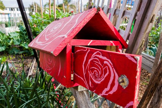 A red wooden letterbox with a white painted floral patern on its roof and door. Found in a community garden in St Kilda, Melbourne.