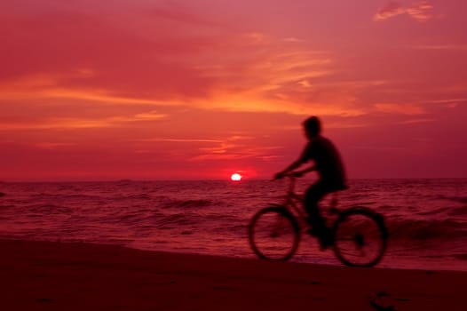 Active. Cyclist on the beach at sundown.