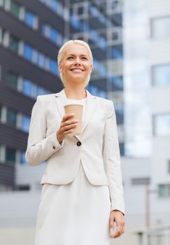 business, hot drinks and people and concept - young smiling businesswoman with paper coffee cup over office building