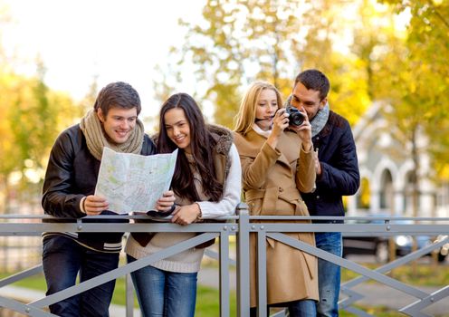 travel, vacation, technology, tourism and friendship concept - group of smiling friends with digital photo camera and map in city park