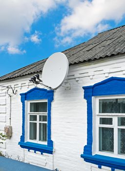 A satellite dish capable of accepting three satellites on the wall of the rural house.