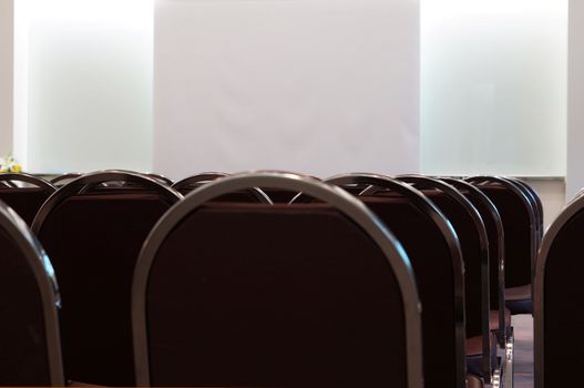 Inside meeting room at office, have many chairs and a screen for slide projector in the middle.                               