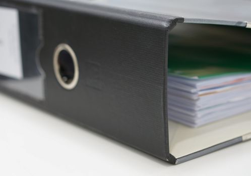 Stack of documents in black binders on desk at office.                        