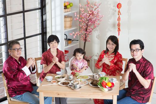 Happy Chinese New Year, reunion dinner. Happy Asian Chinese multi generation family with red cheongsam greeting while dining at home.