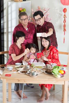 Happy Chinese New Year, taking selfie at reunion dinner. Happy Asian Chinese multi generation family with red cheongsam dining at home.