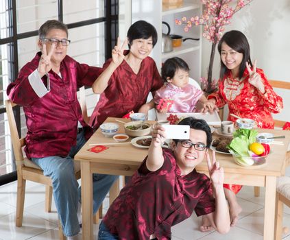 Spring seasons Chinese New Year, reunion dinner. Happy Asian Chinese multi generation family with red cheongsam selfie while dining at home.