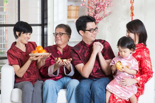 Celebrating Chinese new year. Happy Asian multi generations family in red cheongsam reunion and greeting at home.