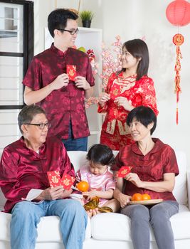 Chinese new year celebration. Happy Asian multi generations family in red cheongsam showing red packets while reunion at home.