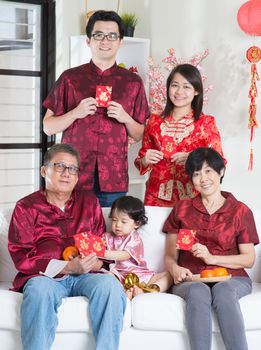 Celebrating Chinese new year. Happy Asian multi generations family in red cheongsam showing red packets while reunion at home.